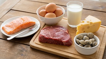 Primer plano de salmón, huevos, leche, queso, carne roja cruda y almejas en recipientes sobre una mesa de madera.