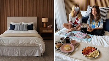 Dos niñas sonrientes, una con camiseta de River Plate y otra de Argentina, desayunan con panqueques y frutas en una cama con respaldo de madera