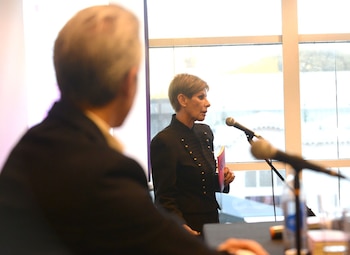 Stella Maris Cuevas, mujer de cabello corto y chaqueta oscura con botones, habla a un micrófono sosteniendo un libro rosa, vista de perfil