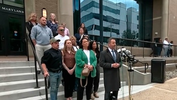 Un grupo de personas, incluyendo a Dwight DJ Rust Jr y Michelle Rust, de pie en escaleras frente a un edificio de Maryland, con un orador en primer plano