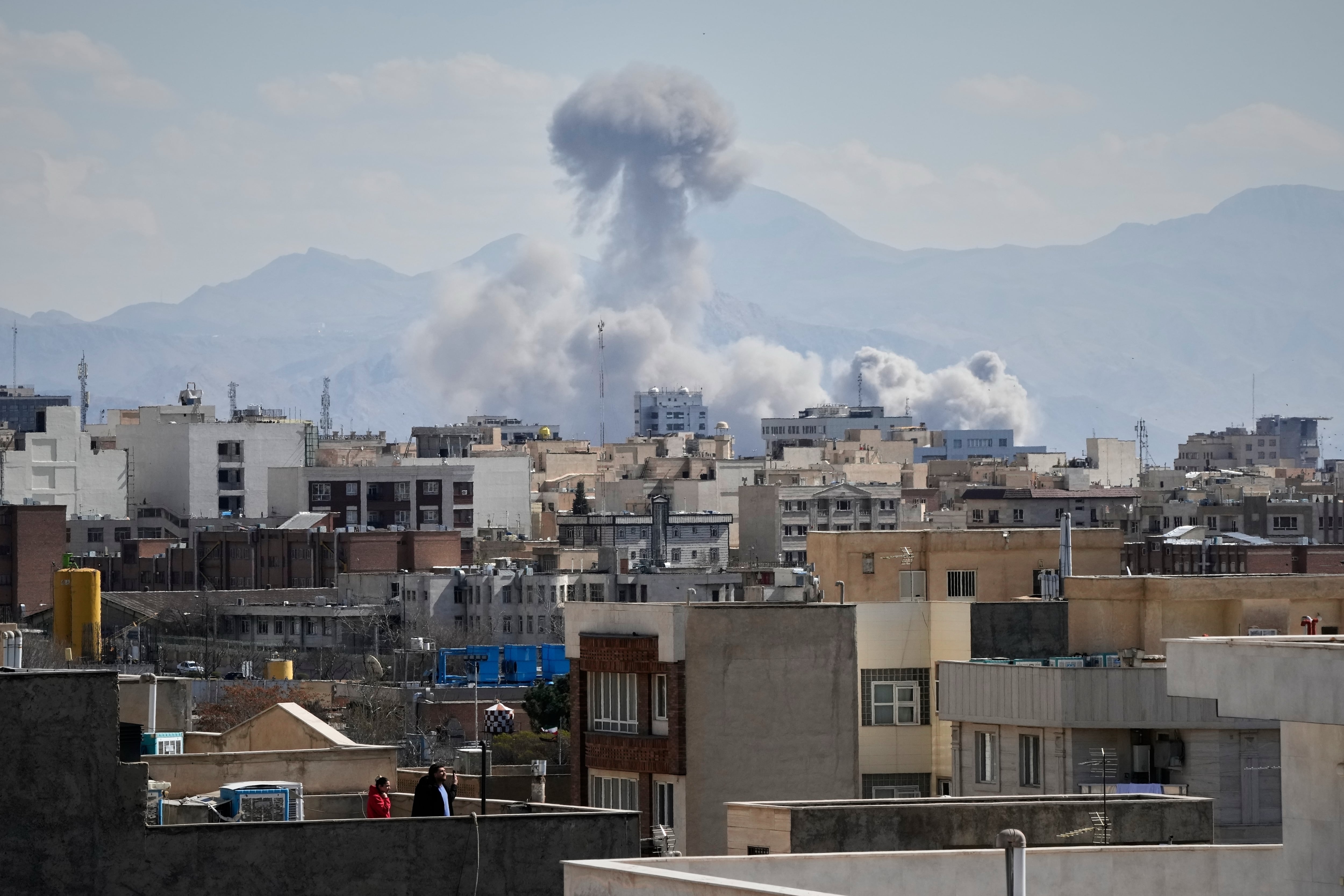 Personas observan desde una azotea mientras una columna de humo se eleva tras un ataque en Teherán, Irán, el domingo 1 de marzo de 2026. (Foto AP/Vahid Salemi)
