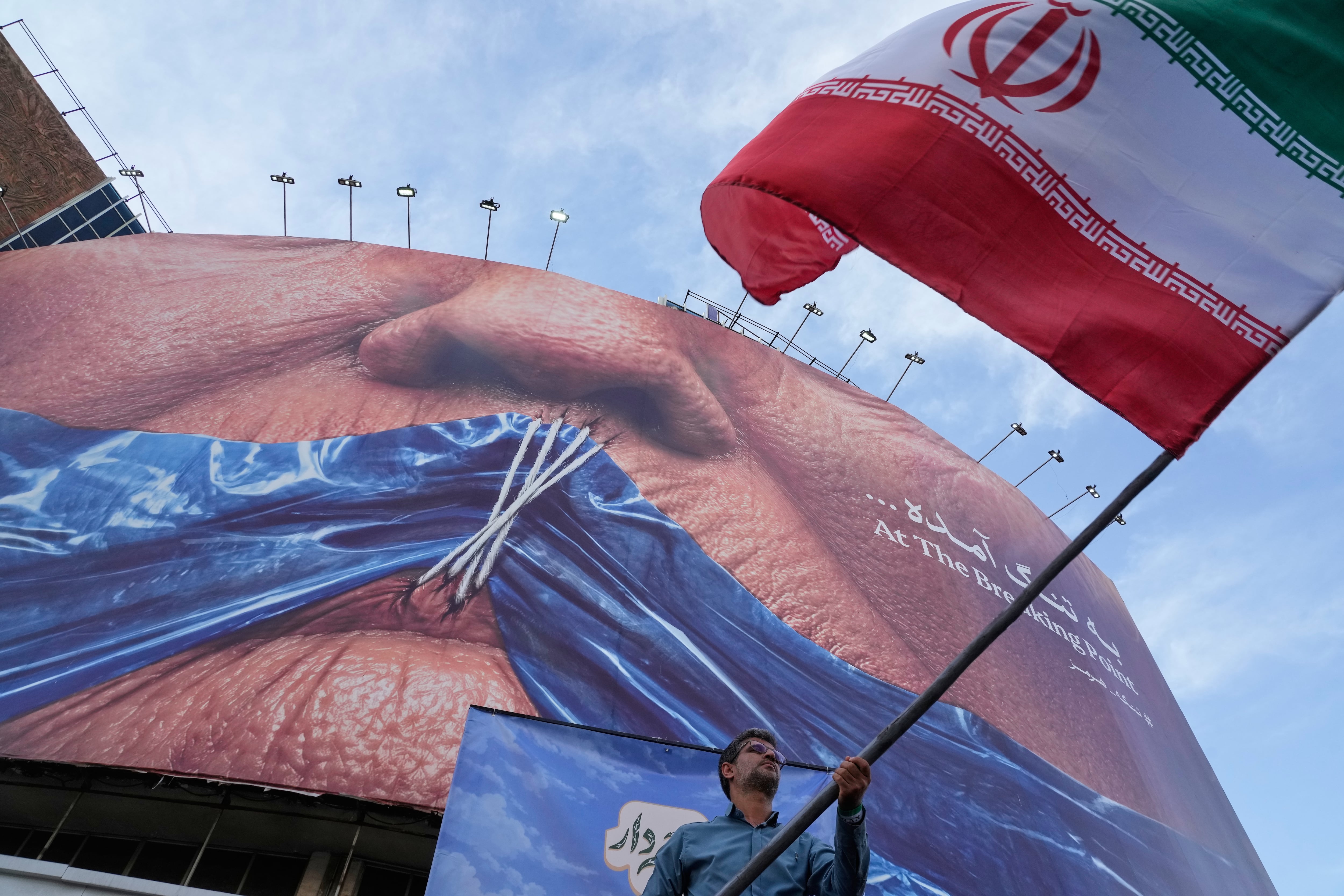 Un hombre agita una bandera iraní durante un acto oficialista en Teherán bajo un cartel propagandístico contra Donald Trump y el estrecho de Ormuz (AP)