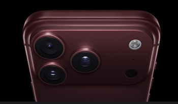 Parte posterior de un teléfono inteligente color granate con tres lentes de cámara, un flash y un sensor sobre fondo negro