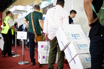 Vista parcial de un pasillo con alfombra roja donde varias personas, incluyendo un guardia de seguridad, mueven cajas marcadas con logotipos de libros