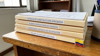 Cuatro carpetas de trámites de construcción con etiquetas impresas y un pin con la bandera de Colombia sobre un escritorio de madera.