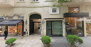 Fachada de un edificio con un portal de arco abierto, escaparates acristalados, faroles de pared y pequeños arbustos en la acera