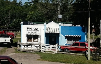 Exterior del Destacamento de Policía "El Peligro" en Berazategui, un edificio blanco y azul con cercado de madera y varios vehículos policiales y civiles en frente