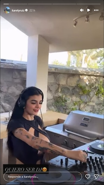 Mujer con cabello oscuro y tatuajes en los brazos usa auriculares y manipula una mesa de mezclas de DJ en un exterior
