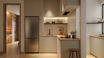 Cocina moderna y compacta con gabinetes claros, refrigerador de acero inoxidable, fregadero, estufa y baldas. Paredes de azulejos cuadrados y suelo de madera clara.