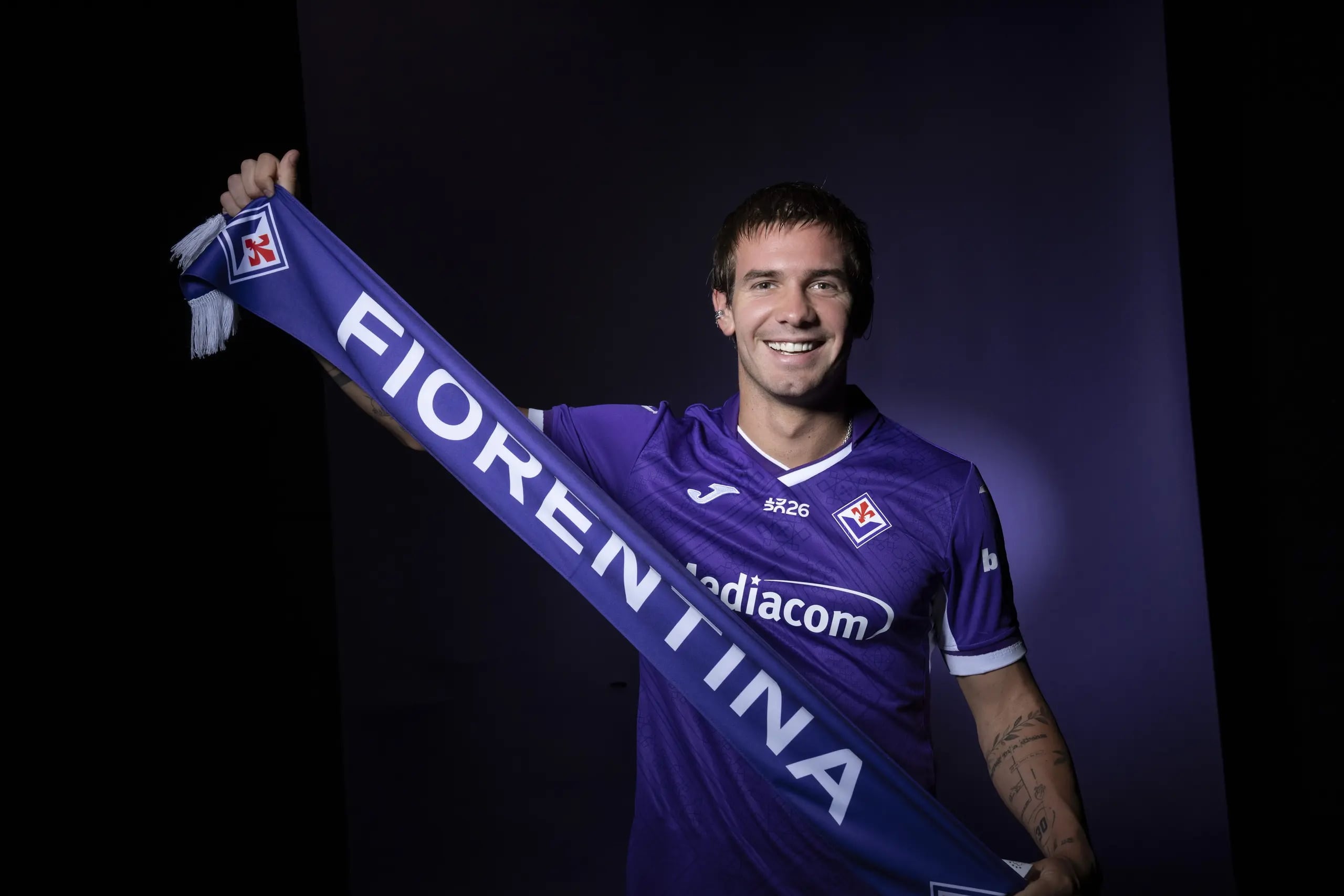 Franco Mastantuono sonríe mientras sostiene una bufanda violeta del club Fiorentina, su nuevo equipo en Italia. (Fiorentina oficial)
