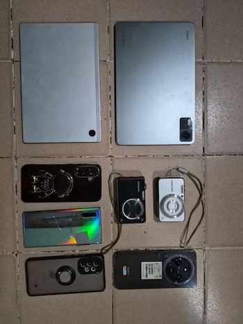 Vista aérea de dos tabletas, tres teléfonos inteligentes y dos cámaras digitales compactas Samsung, dispuestas sobre un suelo de baldosas color crema