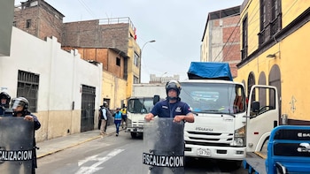 Un agente de fiscalización con casco y escudo transparente permanece de pie en una calle frente a un camión blanco