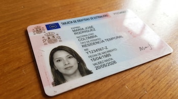 Primer plano de una Tarjeta de Identidad de Extranjero española sobre una mesa de madera clara, mostrando los datos personales y fotografía de una mujer.