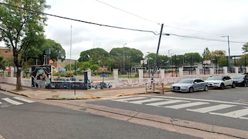 Calle con cruce peatonal frente al Espacio Lavarden en Parque Patricios, mostrando un muro con mural, árboles, juegos infantiles y coches estacionados