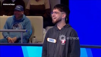 Un hombre con anteojos, barba y buzo gris con el cartel Gonza sonríe frente a un estudio de televisión