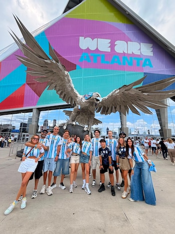 Grupo de personas con camisetas de fútbol de Argentina posa frente a una gran escultura de un águila y la fachada de un estadio con el texto We Are Atlanta