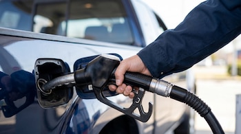 Primer plano de la mano de un hombre insertando una boquilla de gasolina en el tanque de una camioneta pickup azul en una estación de servicio.