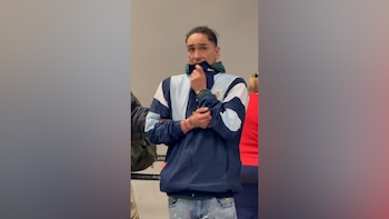 Hombre esposado con una chaqueta deportiva azul y celeste que se cubre la boca con el cuello de la prenda