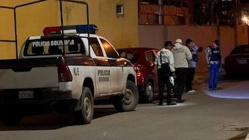 Camionetas de la Policía Boliviana con luces azules y rojas estacionadas en una calle oscura, con agentes y un coche rojo detrás