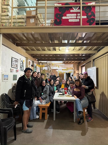 Grupo de aproximadamente veinte personas sonrientes, en su mayoría mujeres, posando para una foto alrededor de una mesa y sillas en un espacio interior con un cartel de AMMAR