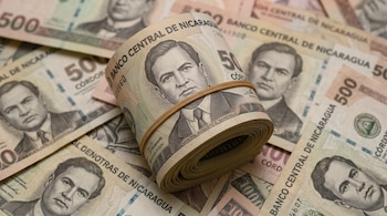 Un fajo enrollado de billetes nicaragüenses atado con una goma elástica sobre billetes extendidos de cien y quinientos córdobas.