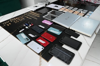 Vista superior de una mesa con laptops, tabletas, teléfonos móviles, unidades USB, varias piezas de joyería de oro y dinero en efectivo