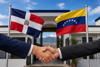 Dos personas con traje se dan la mano frente a las banderas de República Dominicana y Venezuela instaladas en la entrada de un inmueble.