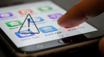 Pantalla de celular con iconos de aplicaciones de bancos, un dedo tocando la pantalla y un símbolo de advertencia triangular.