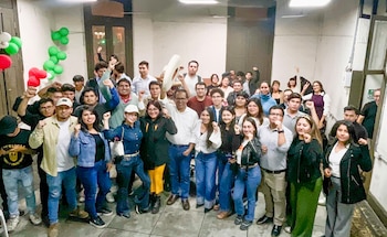Una multitud de personas jóvenes y adultas posa en una sala, la mayoría con los puños en alto, junto a globos rojos, verdes y blancos