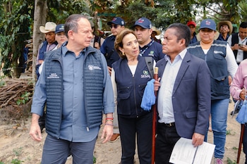 Grupo de personas al aire libre. Un hombre con chaleco azul con texto "Ministro de Desarrollo Social Abelardo Pinto Moscoso", una mujer con chaleco SESAN, y un hombre con traje oscuro y bastón