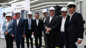 Seis personas con cascos blancos de seguridad en una fábrica con logotipos Fogel y Hoshizaki y una bandera de Estados Unidos