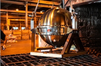 Una gran esfera de metal sobre una estructura con ganchos y cadenas en el interior de una nave industrial