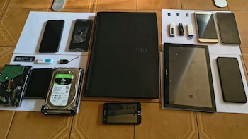 Siete teléfonos inteligentes, una computadora portátil negra, una tableta, tres discos duros, memorias USB y tarjetas de memoria sobre papel