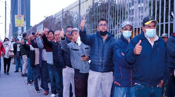 Hombres alineados en una acera junto a una reja metálica, varios con el pulgar hacia arriba y algunos con mascarilla.