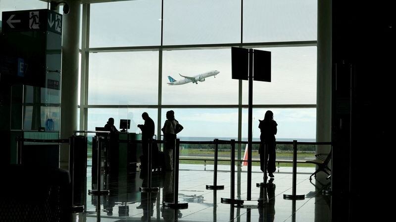 La gente hace fila en el aeropuerto de Barcelona para facturar un vuelo meintras un avión despega en la pista (REUTERS/Jorge Silva)