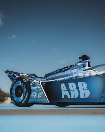 Vista lateral y en ángulo bajo de un automóvil de carreras azul con inscripciones comerciales sobre asfalto y bajo un cielo despejado