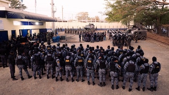 Vista de grupos de agentes de seguridad y soldados en uniformes militares y tácticos reunidos en un patio de tierra con vehículos blindados