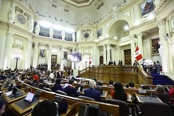 Salón legislativo con legisladores sentados, una tribuna principal con banderas de Perú, una pantalla grande, paredes con esculturas y pinturas decorativas