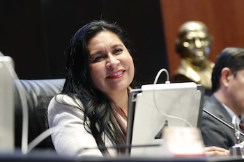 Primer plano de Ana Lilia Rivera, mujer de cabello oscuro y labios rojos, sonriendo levemente mientras mira hacia la derecha, con un dispositivo blanco frente a ella