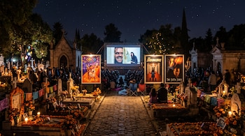 Un cementerio de noche con tumbas iluminadas por velas, personas sentadas frente a una pantalla de cine y tres carteles de películas.
