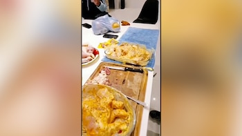 Mesa con pollo crudo, pollo marinado en dos recipientes de vidrio, tabla de cortar con restos de carne, un cuchillo, dos teléfonos móviles y una bolsa de plástico