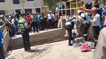 Policías y rescatistas con equipo especializado se congregan junto a un canal de agua; una multitud de personas observa la escena en el fondo