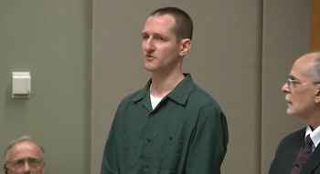 Hombre de cabello corto y barba escasa vestido con camisa verde en un tribunal, junto a un hombre con traje oscuro y corbata