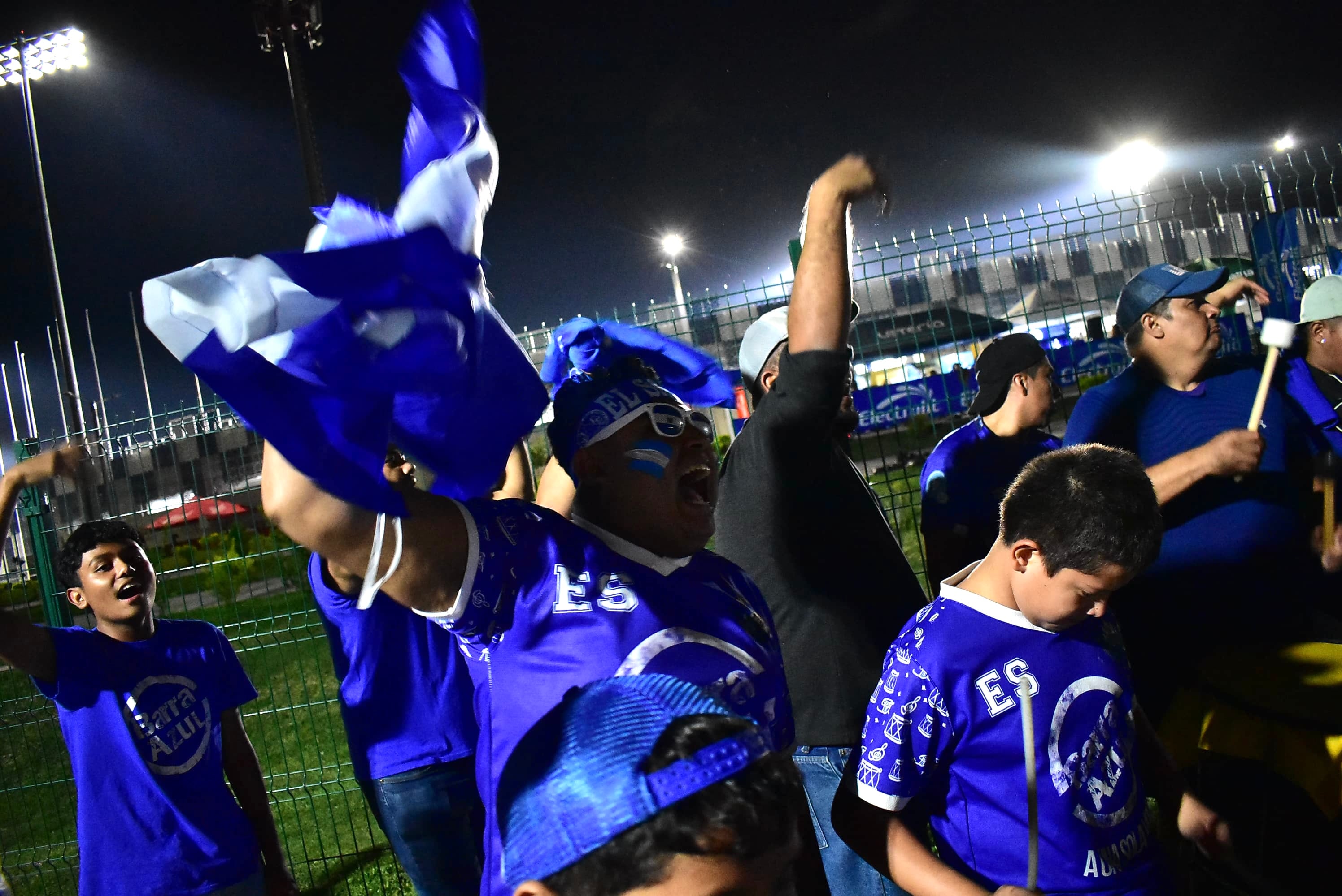 Un grupo de seguidores de la selección de fútbol de El Salvador ondea banderas y toca instrumentos durante un encuentro nocturno, alegría para toda la familia. (Infobae Centroamérica/Emerson Del Cid)