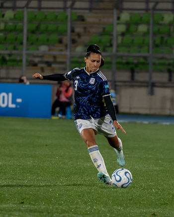 Once jugadoras de la Selección Femenina de Argentina posan sonrientes en el campo de un estadio por la noche, vistiendo uniformes oscuros con detalles celestes y blancos