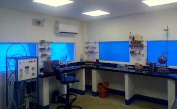 Interior de un laboratorio con encimeras, fregadero, silla, estantes con material de vidrio, un purificador de agua y ventanas con fondo azul