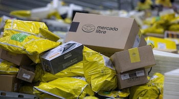 Vista de cerca de numerosos paquetes y cajas, principalmente amarillos, apilados en un centro de clasificación. Una caja grande con el logo de Mercado Libre es visible en el centro.