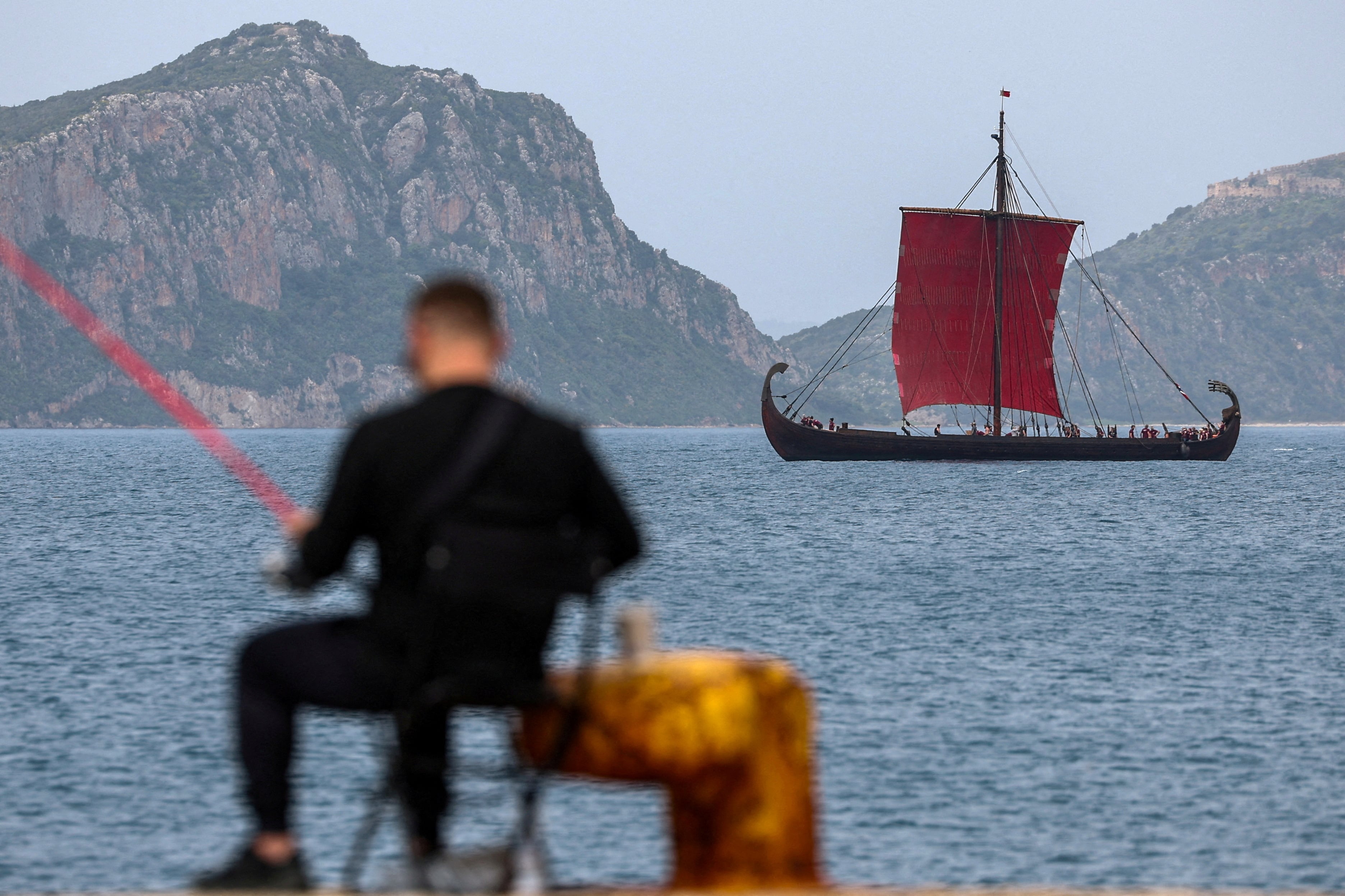 Un hombre pesca mientras se ve al fondo una réplica de un antiguo buque de guerra, durante el rodaje de La Odisea, el último proyecto del director Christopher Nolan, en la ciudad de Pilos, Grecia, en marzo de 2025.(Foto: REUTERS/Louisa Gouliamaki)
