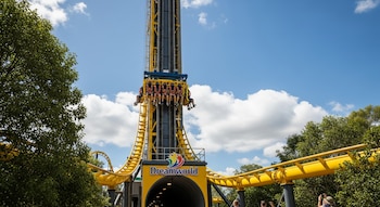 Vista de la Tower of Terror II en Dreamworld con personas en el vehículo a gran altura, estructura amarilla y negra, cielo azul con nubes y árboles verdes.