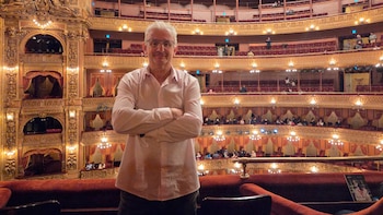 Sergio Kuchevasky, hombre de cabello blanco y lentes, sonríe con los brazos cruzados frente al interior ornamentado del Teatro Colón